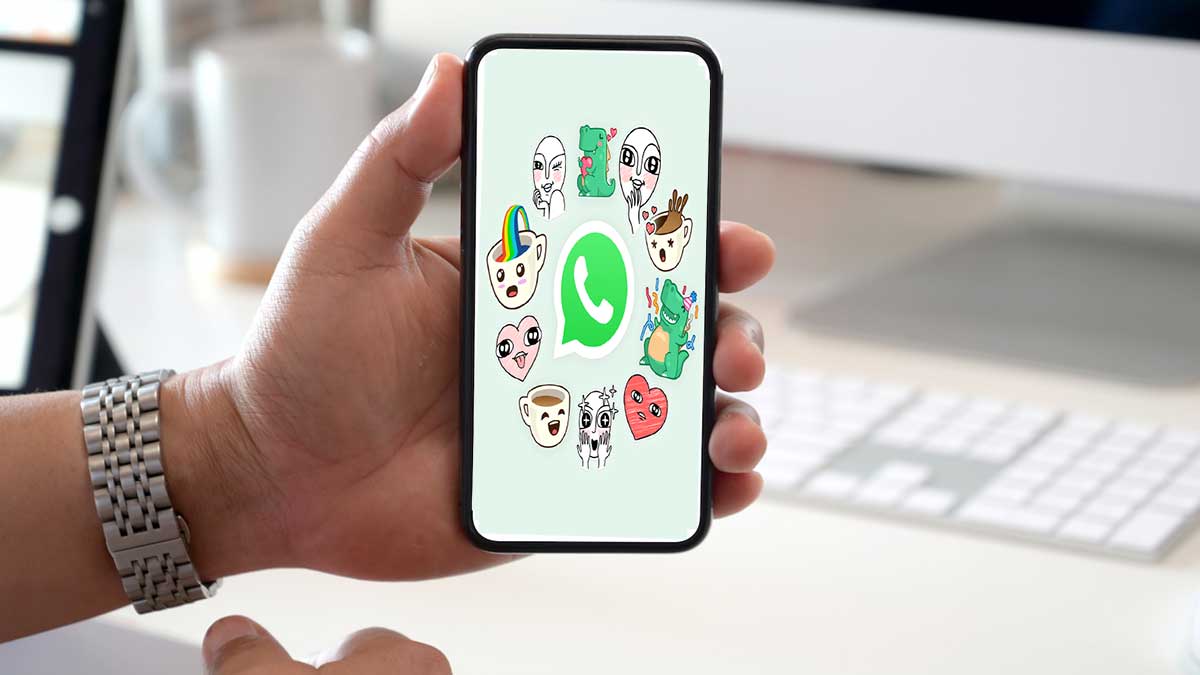 Una persona sujetando un móvil con el logo de WhatsApp y unos stickers en la pantalla.