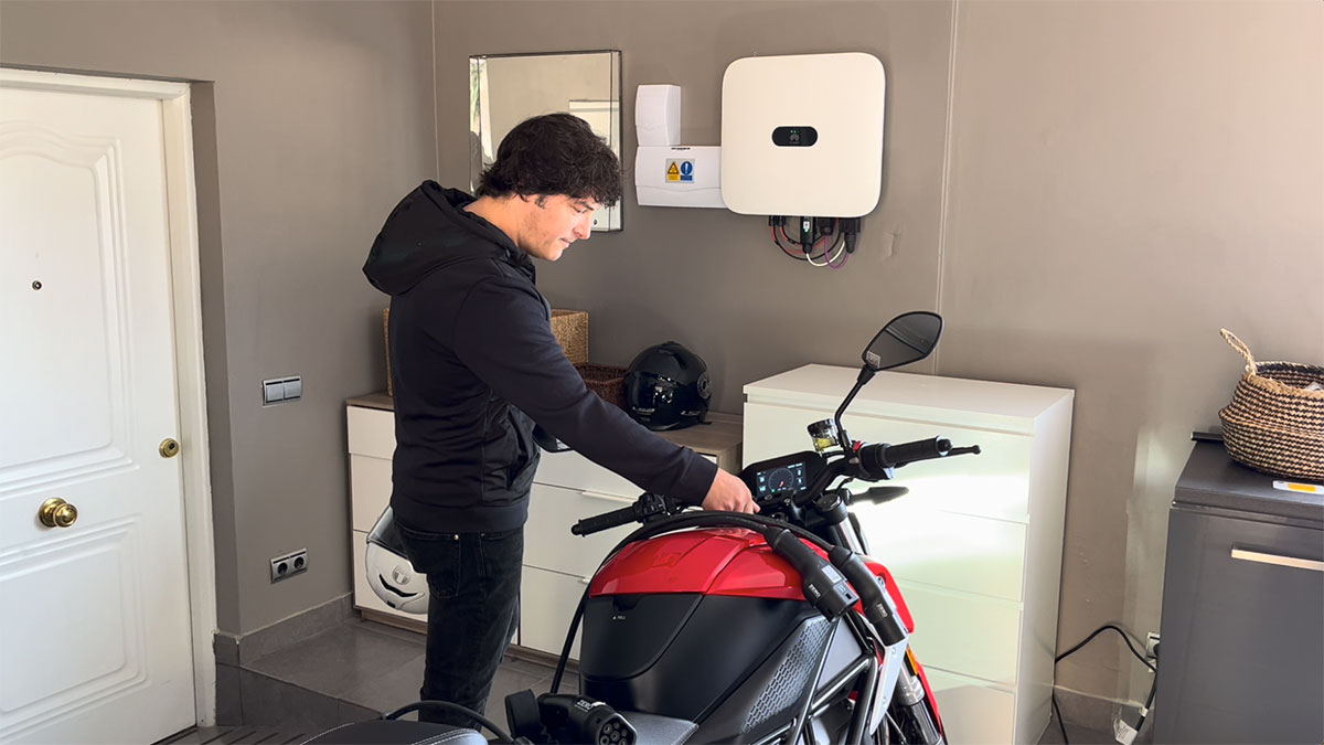 Jordi Cruz en su casa junto a su moto eléctrica y el inversor de sus placas solares.