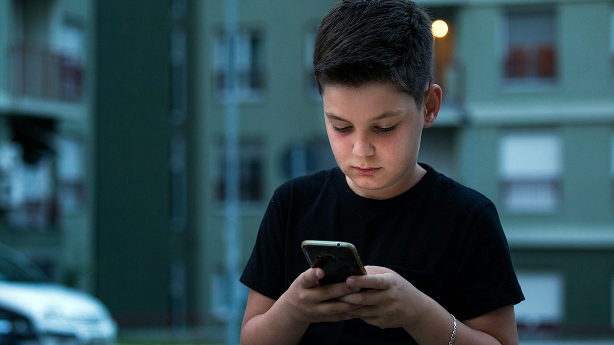 Un niño en la calle con un teléfono móvil.