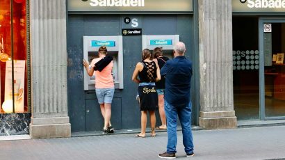 Una entidad bancaria en la calle con gente sacando dinero de los cajeros automáticos.