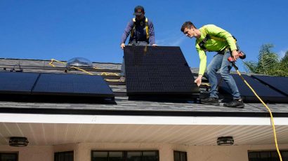 Unos operarios instalando paneles solares en el tejado de una casa.