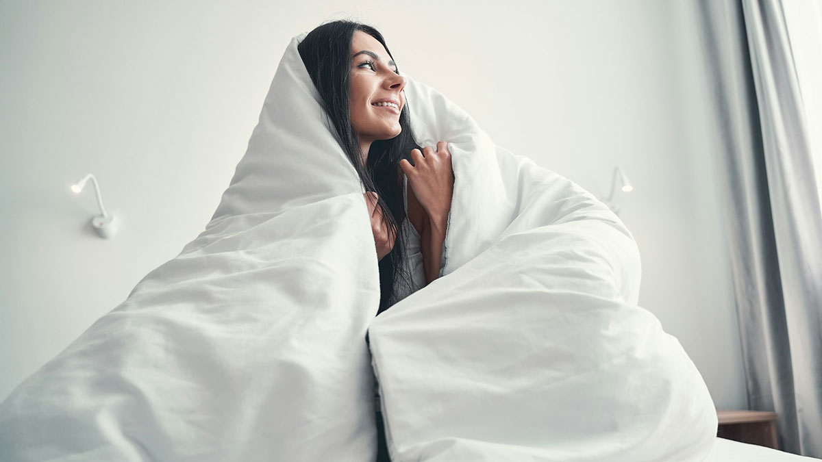 Una mujer arropada con el edredón de la cama.