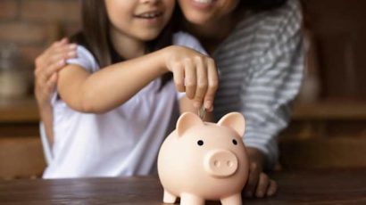 Una madre con su hija metiendo una moneda en una hucha.