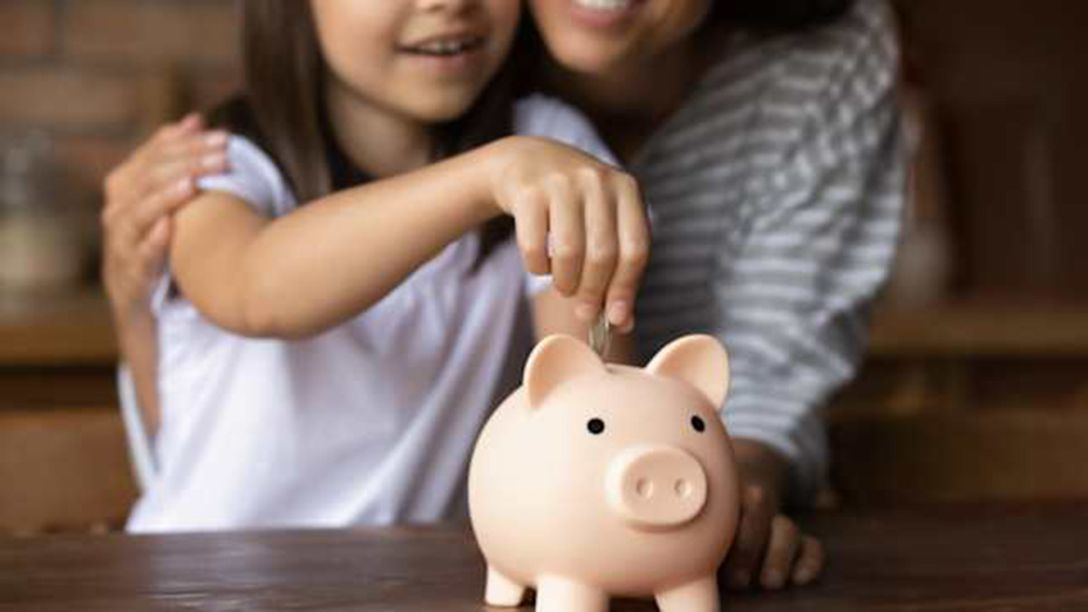 Una madre con su hija metiendo una moneda en una hucha.