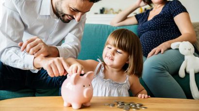 Una niña pequeña con sus padres metiendo monedas en una hucha.