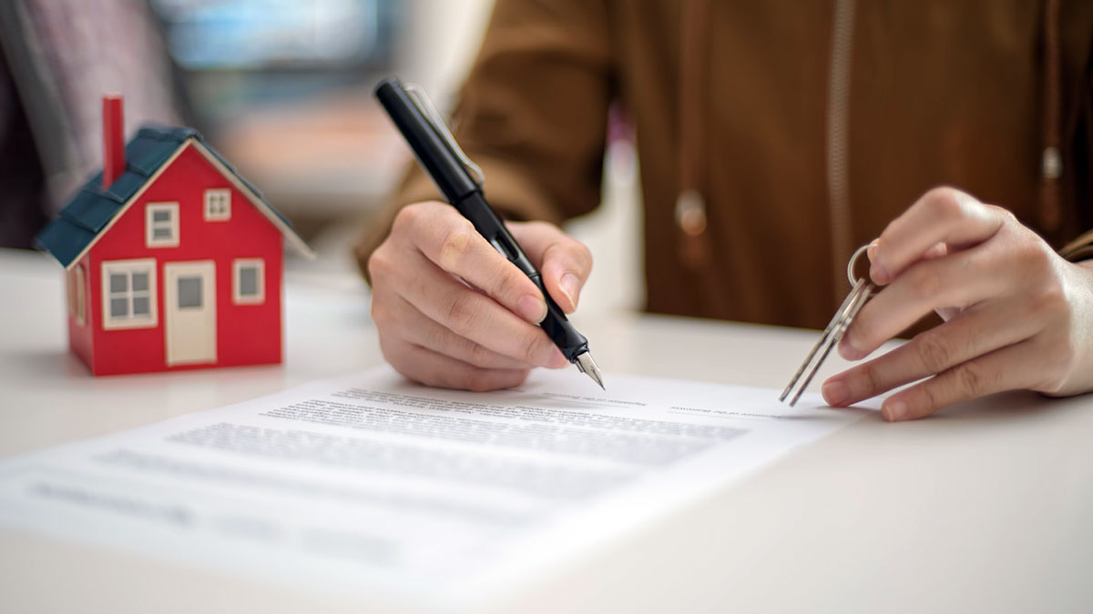 Una persona firmando un contrato de alquiler de una casa.