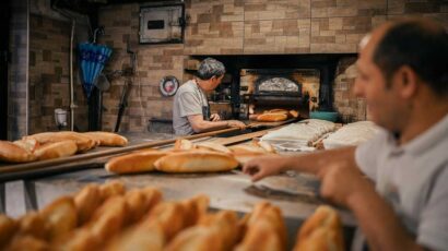 Unos panaderos elaboran barras de pan en un horno.