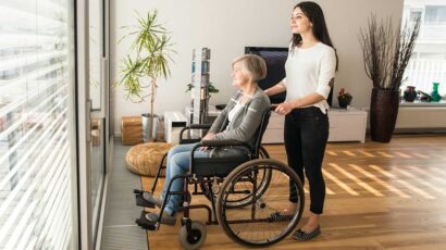 Una mujer cuidando de una persona mayor en silla de ruedas.